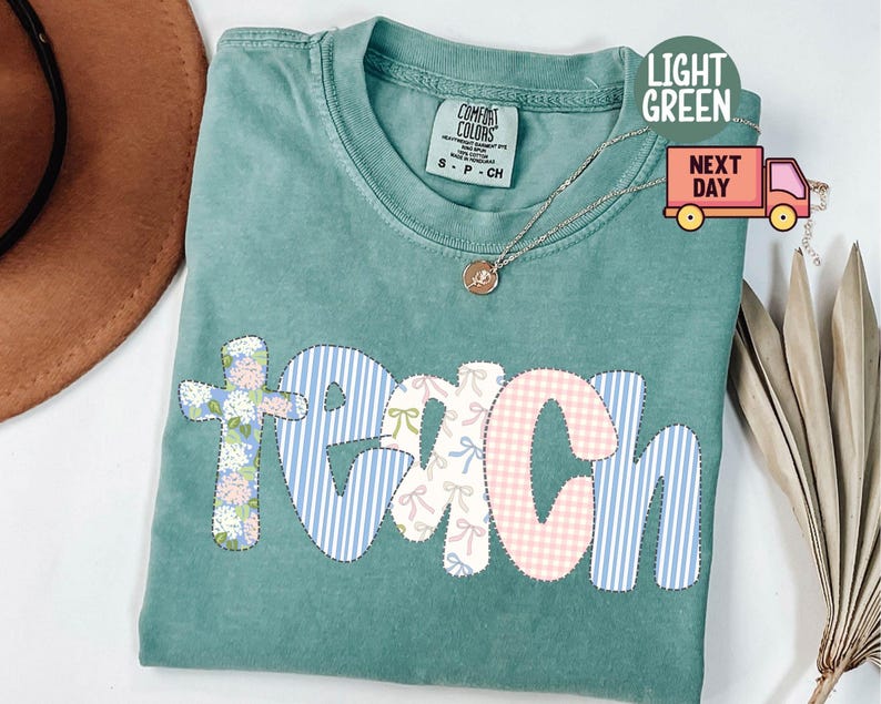 May include: Light green Comfort Colors t-shirt with the word "TEACH" in a patchwork design. The letters are decorated with floral, striped, and gingham patterns. A gold necklace with a pendant is visible.