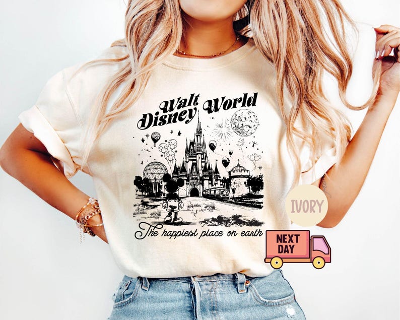 May include: Ivory-colored t-shirt featuring a black and white graphic of Walt Disney World. The design includes Cinderella's castle, Mickey Mouse, balloons, and the text "The happiest place on earth."