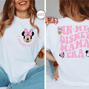 May include: White t-shirt with a Minnie Mouse graphic on the front and the text "DISNEY MAMA". The back of the shirt features the text "IN MY DISNEY MAMA ERA" with additional Disney character graphics in pink.