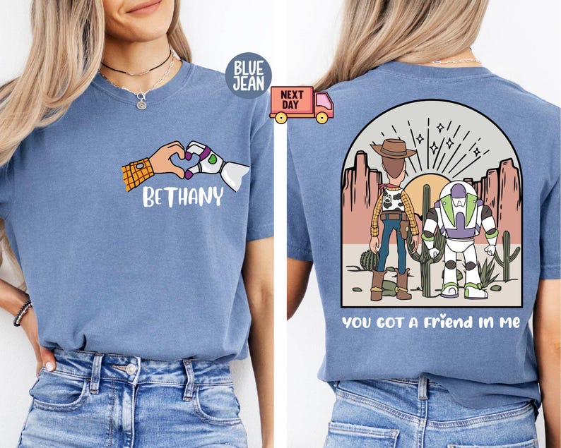 Pu&ograve; includere: Una t-shirt blu con una grafica frontale di una mano umana e una mano robotica che formano un cuore sopra il nome BETHANY. La grafica sul retro mostra due personaggi dei cartoni animati in un deserto con il testo YOU GOT A FRIEND IN ME.