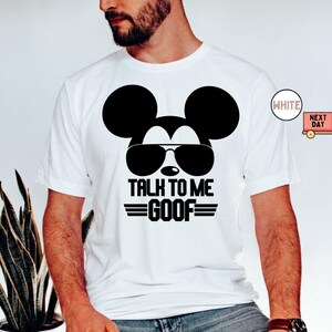 May include: A white short-sleeved t-shirt featuring a black graphic of a mouse head wearing sunglasses. Below the graphic, the text reads TALK TO ME GOOF in bold black capital letters, flanked by two horizontal lines on each side of the word GOOF.