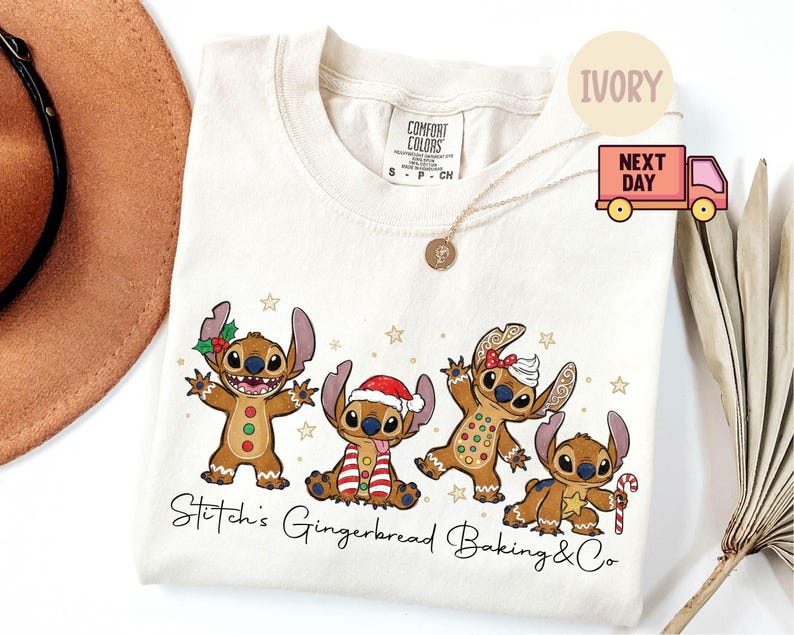 Puede incluir: Camiseta de color marfil con un dise&ntilde;o festivo de cuatro personajes Stitch estilo pan de jengibre. Los personajes est&aacute;n decorados con accesorios navide&ntilde;os y rodeados de estrellas. El texto "Stitch's Gingerbread Baking & Co" est&aacute; impreso debajo.