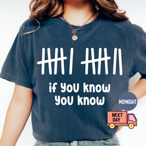 May include: Navy blue t-shirt with white tally marks and the phrase "if you know you know" in a bold, sans-serif font. The shirt has a classic crew neck and short sleeves. A small graphic of a delivery truck is visible.
