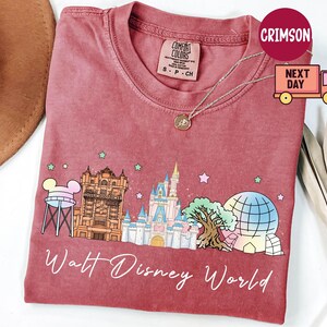 May include: A red t-shirt featuring a colorful graphic of Walt Disney World landmarks, including Cinderella's castle, the Tower of Terror, and Spaceship Earth. The words "Walt Disney World" are written in a cursive font below the graphic.