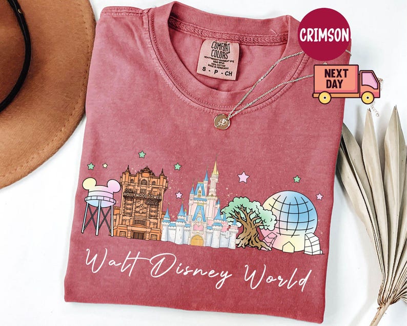 May include: A red t-shirt featuring a colorful graphic of Walt Disney World landmarks, including Cinderella's castle, the Tower of Terror, and Spaceship Earth. The words "Walt Disney World" are written in a cursive font below the graphic.