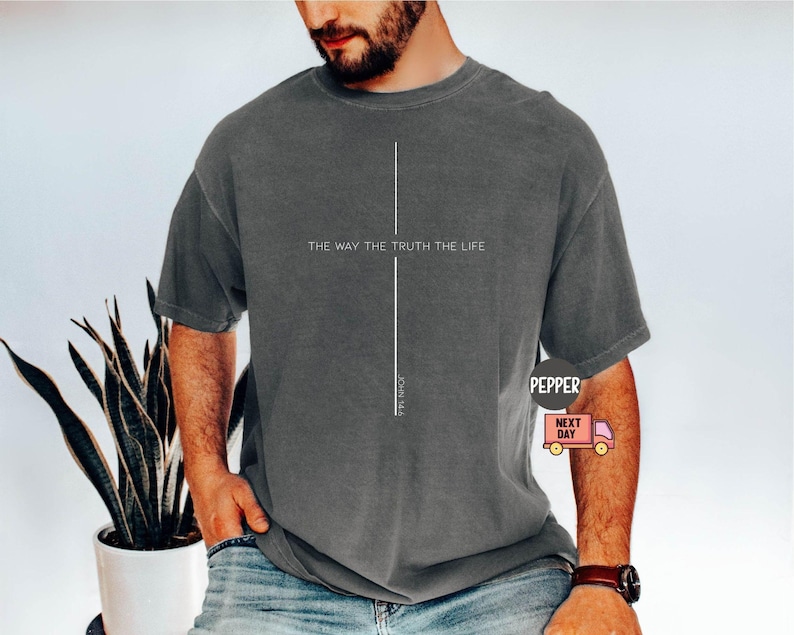 Puede incluir: Camiseta gris oscuro con el texto "THE WAY THE TRUTH THE LIFE" y un dise&ntilde;o de l&iacute;nea vertical. La camiseta se lleva con vaqueros azules. Tambi&eacute;n es visible el texto "JOHN 14:6".