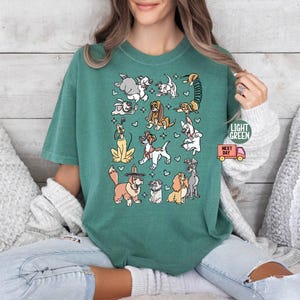 May include: Light green t-shirt featuring a collection of cartoon dog illustrations. The dogs are in various poses and breeds, with small hearts scattered around them. The shirt has the text "LIGHT GREEN" and a small delivery truck graphic.