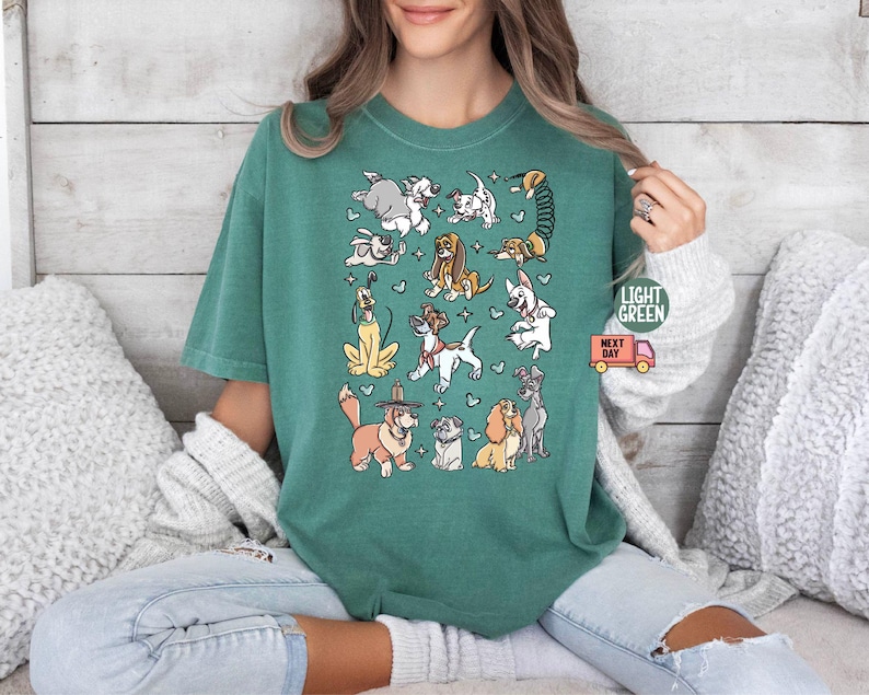 May include: Light green t-shirt featuring a collection of cartoon dog illustrations. The dogs are in various poses and breeds, with small hearts scattered around them. The shirt has the text "LIGHT GREEN" and a small delivery truck graphic.