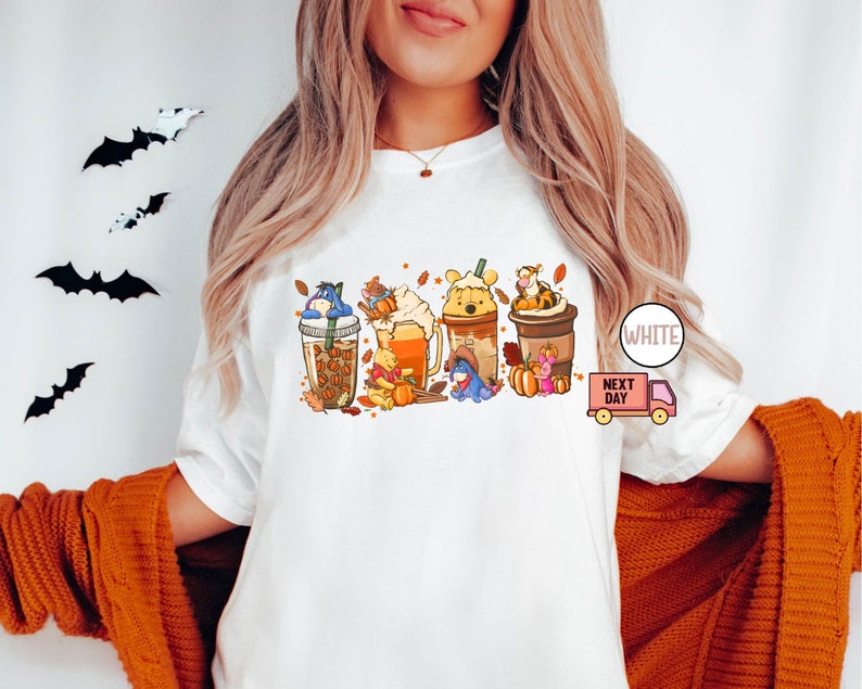 May include: White t-shirt featuring a colorful graphic of fall-themed coffee drinks, each adorned with a different character. The design includes pumpkins, leaves, and the text "WHITE" and "NEXT DAY".