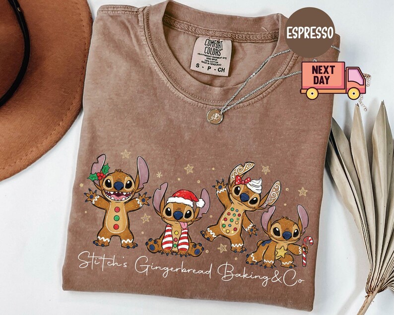 Puede incluir: Camiseta color espresso con un dise&ntilde;o de Stitch estilo pan de jengibre y detalles festivos. La camiseta tiene el texto "Stitch's Gingerbread Baking & Co". La camiseta es de la marca Comfort Colors.