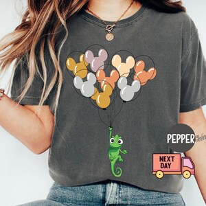 Może przedstawiać: Szary T-shirt z grafiką przedstawiającą kameleona trzymającego wiązkę kolorowych balon&oacute;w w kształcie Myszki Miki. Na czerwonym samochodzie ciężarowym nadrukowany jest napis "Next Day".