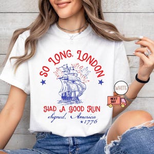 May include: White t-shirt with a nautical design featuring a ship, fireworks, and text that reads "So Long, London, Had a Good Run, Signed, America, *1776". The design includes red, white, and blue elements.