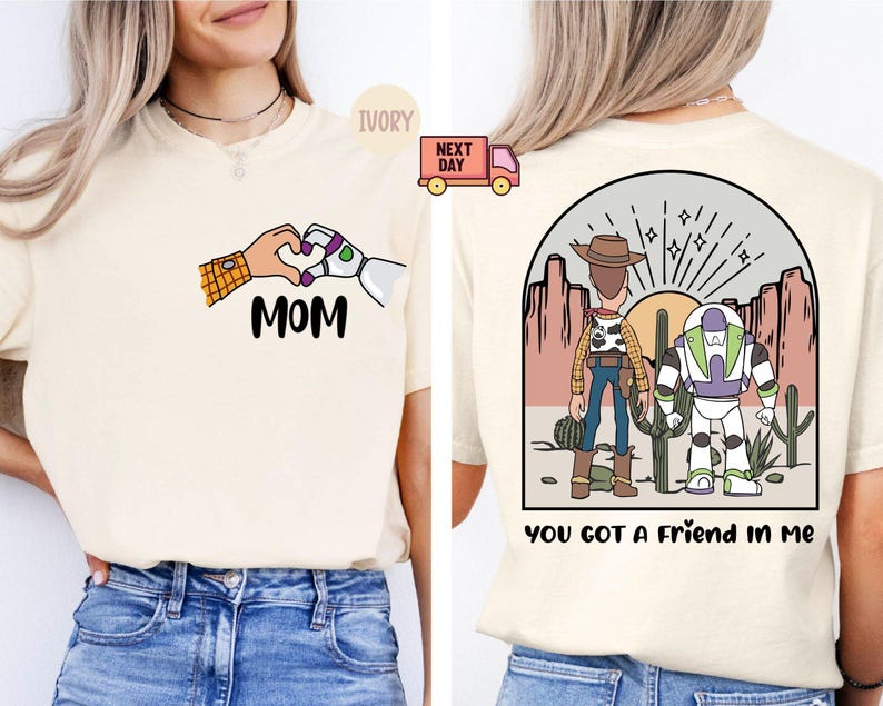 Pu&ograve; includere: Una t-shirt color avorio con una grafica frontale di due mani che formano un cuore sopra la scritta MOM. La grafica sul retro mostra una scena nel deserto con due personaggi dei cartoni animati davanti a un sole, con la scritta YOU GOT A FRIEND IN ME.