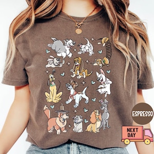 May include: Espresso-colored t-shirt featuring a collection of cartoon dogs in various poses. The dogs are in different colors and styles, with stars and hearts scattered around them. The shirt has a crew neck and short sleeves.