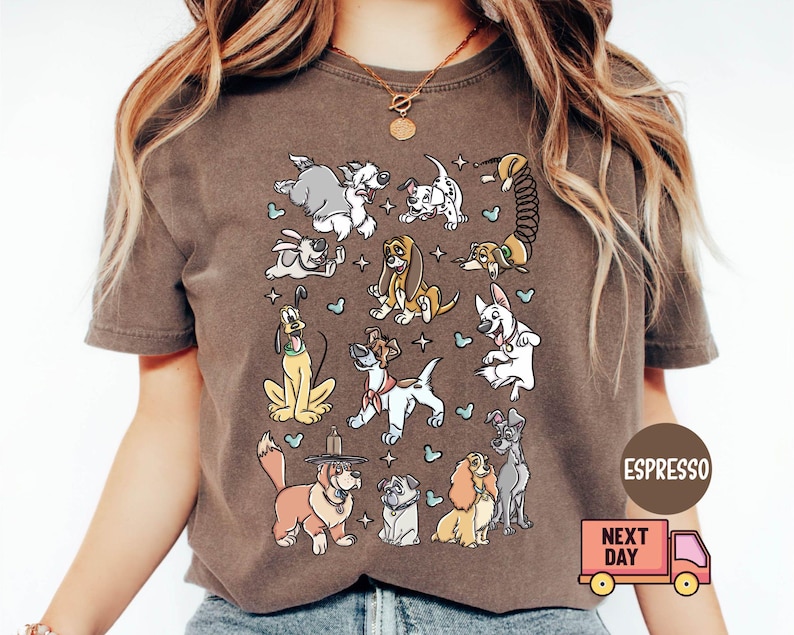 May include: Espresso-colored t-shirt featuring a collection of cartoon dogs in various poses. The dogs are in different colors and styles, with stars and hearts scattered around them. The shirt has a crew neck and short sleeves.