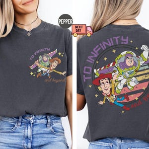 May include: A dark gray t-shirt with a graphic print of Woody and Buzz Lightyear from Toy Story. The graphic features the characters flying through space with the text "To Infinity and Beyond".