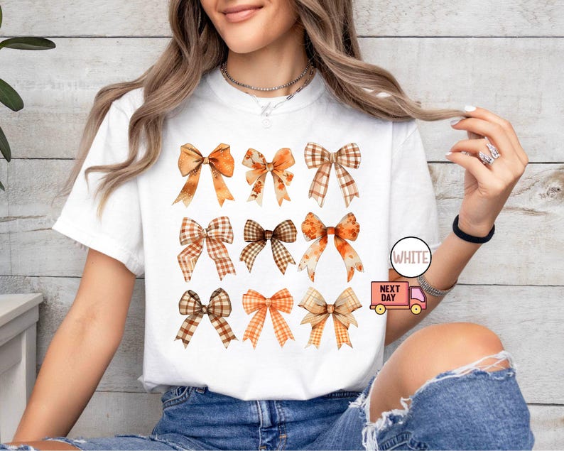 May include: White t-shirt with a design of nine brown and orange bows with plaid patterns. The shirt is on a model wearing blue jeans.
