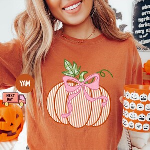 May include: Orange t-shirt with a pumpkin graphic, pink bow, and green leaves. An orange mug with jack-o'-lantern faces is held. A small orange pumpkin bucket is also visible. The text on the sign says "when we're together darling every night is halloween".