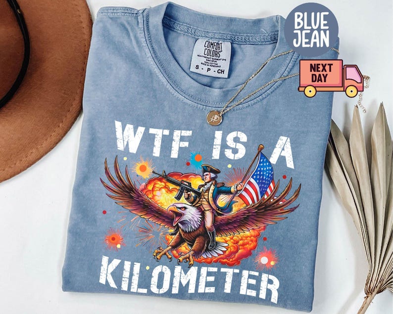 May include: Blue jean t-shirt with the text "WTF IS A KILOMETER". The graphic features an eagle carrying a soldier with a rifle and an American flag. The shirt is a Comfort Colors brand.