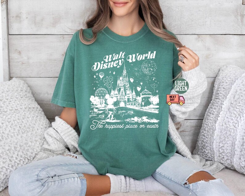 May include: Light green t-shirt with a white graphic of the Walt Disney World castle, Mickey Mouse, and other park elements. The text "Walt Disney World" and "The happiest place on earth" are printed on the shirt.