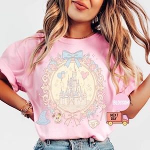K&ouml;nnte beinhalten: Rosa T-Shirt mit einer pastellfarbenen Illustration von Schloss Aschenputtel, umgeben von Blumen und einer Schleife. Der Text "Next Day" befindet sich auf einem rosafarbenen LKW.