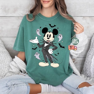 May include: Light green t-shirt featuring a Halloween-themed Mickey Mouse design. Mickey is dressed in a black and white pinstripe suit, surrounded by bats and ghosts. The shirt has the words "Light Green" and "Next Day" printed on it.