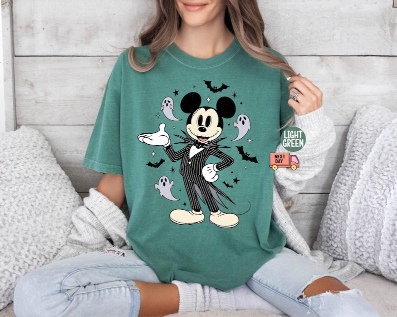 May include: Light green t-shirt featuring a Halloween-themed Mickey Mouse design. Mickey is dressed in a black and white pinstripe suit, surrounded by bats and ghosts. The shirt has the words "Light Green" and "Next Day" printed on it.