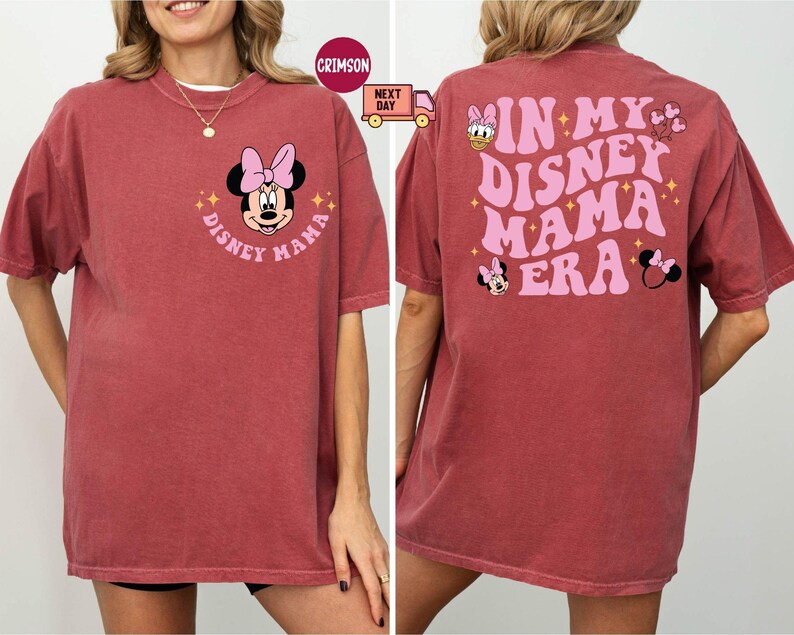 May include: A maroon t-shirt featuring Minnie Mouse with the text "Disney Mama" on the front. The back of the shirt displays the phrase "In My Disney Mama Era" with additional Disney character graphics.