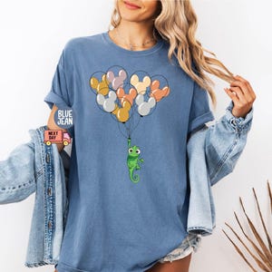 May include: A blue t-shirt with a green chameleon holding onto a bunch of colorful balloons shaped like Mickey Mouse heads.