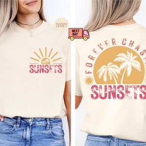 May include: Ivory-colored t-shirt with a sunset graphic on the front and back. The front features a sun with the word "SUNSETS" in pink. The back has a sunset with palm trees and the words "FOREVER CHASING SUNSETS".