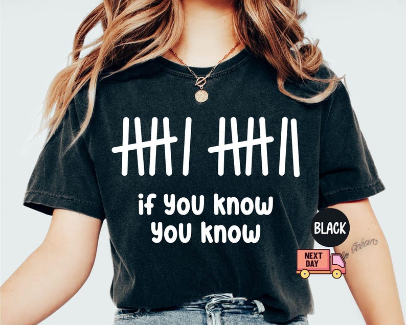 May include: Black t-shirt with white tally marks and the phrase "if you know, you know." The shirt has a crew neck and short sleeves. A black circle with the word "BLACK" is on the right side of the shirt.