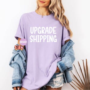 May include: A lavender t-shirt with the text "Upgrade Shipping" in white lettering.