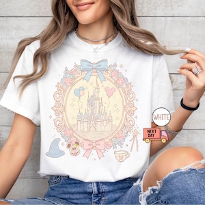 K&ouml;nnte beinhalten: Wei&szlig;es T-Shirt mit einer pastellrosa, blauen und gelben Illustration von Schloss Aschenputtel, Mickey Mouse und anderen Disney-Charakteren. Der Text "WHITE" und "NEXT DAY" ist auf dem Bild zu sehen.