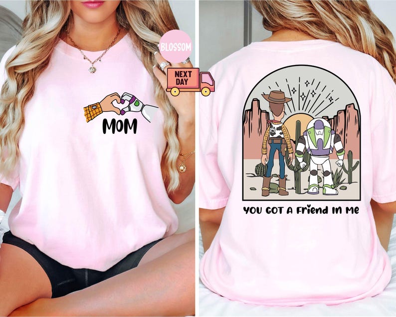 Pu&ograve; includere: Una t-shirt rosa chiaro con una grafica frontale di due mani che formano un cuore con il testo MOM e una grafica sul retro di due personaggi dei cartoni animati in un paesaggio desertico con il testo YOU GOT A FRIEND IN ME stampato sotto.