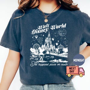 May include: Dark blue t-shirt featuring a white graphic of the Walt Disney World castle, Mickey Mouse, and fireworks. Text reads "Walt Disney World" and "The happiest place on earth".