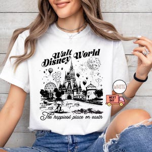 May include: White t-shirt featuring a black and white graphic of Walt Disney World. The design includes the castle, Mickey Mouse, balloons, and fireworks. Text reads "Walt Disney World" and "The happiest place on earth."