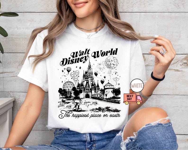 May include: White t-shirt featuring a black and white graphic of Walt Disney World. The design includes the castle, Mickey Mouse, balloons, and fireworks. Text reads "Walt Disney World" and "The happiest place on earth."