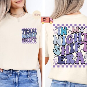 Peut inclure: Un t-shirt blanc avec un motif violet, bleu et rose qui dit "Team Night Shift" sur le devant et "In My Night Shift Era" au dos. Le motif a un fond à carreaux.