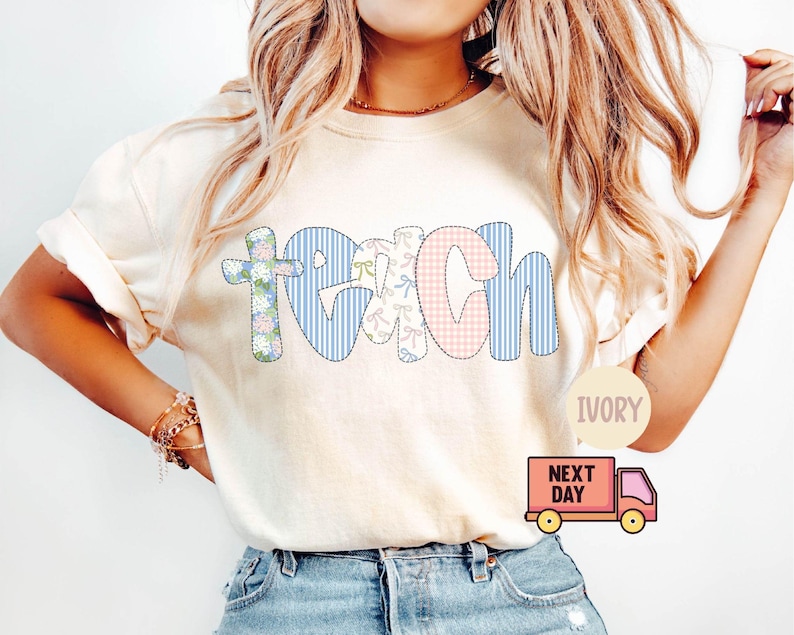 May include: Ivory-colored t-shirt with the word "TEACH" in a patchwork design. The letter "T" is a floral cross, "E" has bows, "A" is pink gingham, "C" and "H" are blue stripes. The shirt has rolled-up sleeves.