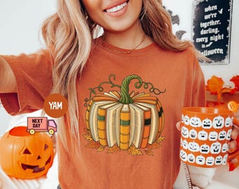 Könnte beinhalten: Orangefarbenes T-Shirt mit einem Kürbis aus Büchern, einem grünen Stiel und Ranken. Das Bild zeigt auch einen kürbisförmigen Süßigkeitenhalter und eine Tasse mit Jack-o'-Laternen-Gesichtern. Der Text auf dem Schild lautet "when we're together darling every night is halloween."
