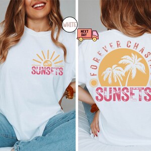 May include: White t-shirt with a front graphic of a sunset and the word "SUNSETS" in pink. The back of the shirt features a larger design with the text "FOREVER CHASING SUNSETS" around a sunset and palm trees.
