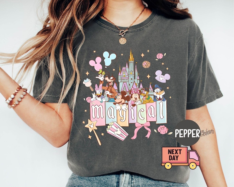 May include: Dark gray t-shirt featuring a colorful graphic with Disney characters and the word "magical." The design includes Mickey and Minnie Mouse, Donald Duck, and a castle. A popcorn box and a magic wand are also included.