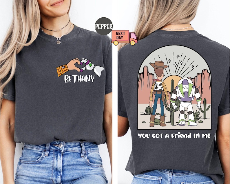 Pu&ograve; includere: Una t-shirt grigio antracite con una grafica frontale di due mani che formano un cuore con il nome BETHANY sotto. La grafica sul retro mostra una scena nel deserto con due personaggi dei cartoni animati e il testo YOU GOT A FRIEND IN ME.