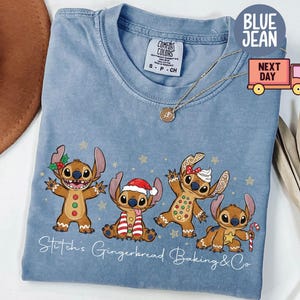 Puede incluir: Una camiseta azul claro Comfort Colors con un dise&ntilde;o de Stitch de pan de jengibre. El dise&ntilde;o incluye cuatro personajes Stitch de pan de jengibre con accesorios festivos y el texto "Stitch's Gingerbread Baking & Co."