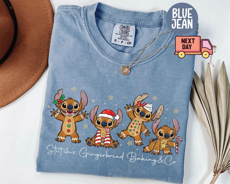 Puede incluir: Una camiseta azul claro Comfort Colors con un dise&ntilde;o de Stitch de pan de jengibre. El dise&ntilde;o incluye cuatro personajes Stitch de pan de jengibre con accesorios festivos y el texto "Stitch's Gingerbread Baking & Co."