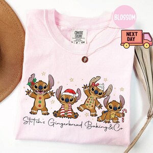 Puede incluir: Camiseta rosa claro con un dise&ntilde;o de cuatro personajes Stitch de jengibre con decoraciones navide&ntilde;as. El texto "Stitch's Gingerbread Baking & Co" est&aacute; impreso debajo. Cuello redondo.