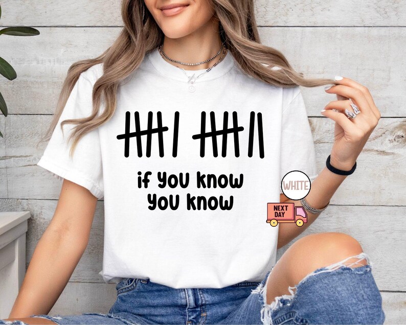 May include: White t-shirt with black tally marks and the phrase "if you know you know." The shirt has a crew neck and short sleeves. The text is in a bold, sans-serif font.