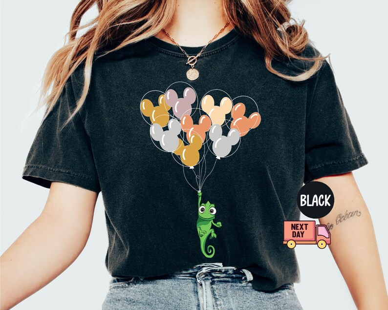 Może przedstawiać: Czarny T-shirt z zielonym kameleonem trzymającym wiązkę kolorowych balon&oacute;w z uszami Myszki Miki. Balony są ż&oacute;łte, pomarańczowe, czerwone, r&oacute;żowe i fioletowe.