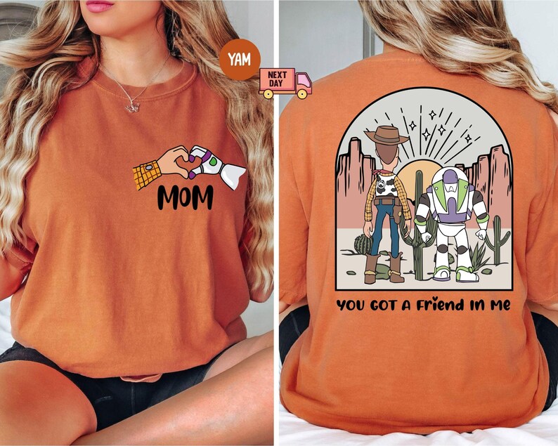 Pu&ograve; includere: Una t-shirt arancione con una grafica frontale di due mani che formano un cuore con il testo MOM sotto. La grafica sul retro raffigura due personaggi dei cartoni animati in un paesaggio desertico con il testo YOU GOT A FRIEND IN ME.
