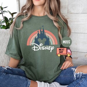 May include: A green t-shirt with a retro rainbow and a silhouette of Cinderella's castle with Mickey Mouse ears. The text "DISNEY" is printed below the castle.